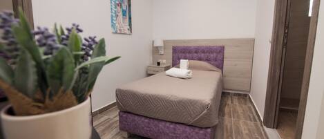 A modern bedroom with a bed, a nightstand, a lamp, and a potted plant.