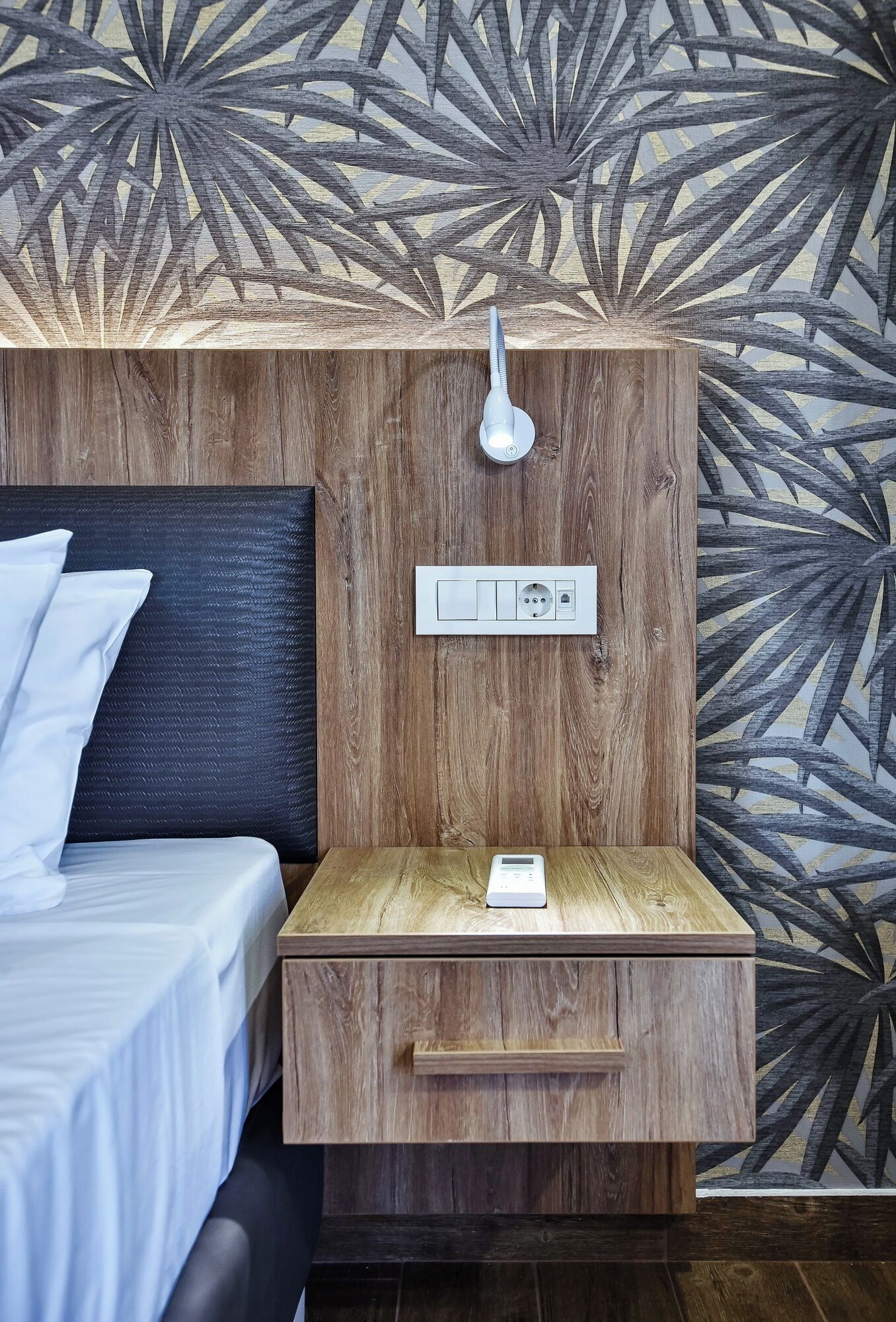 A bedroom with a bed, a nightstand with a lamp, and a power outlet.