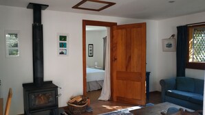 A cozy living room with a wood-burning stove, a blue sofa, and a dining table. - A comfortable, private, country apartment. 300mts walk to safe sandy beach. (Collingwood)
