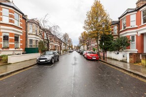 A residential street lined with terraced houses, a wet road, and parked cars. - Lovely 4 Bedroom House near Portobello (London)