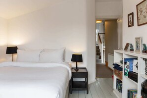 A bedroom with a bed, bedside lamps, a nightstand, and a bookshelf with books and decorative items. - Lovely 4 Bedroom House near Portobello (London)