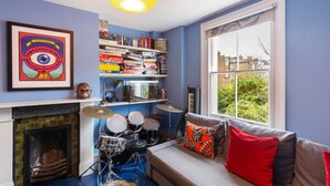 Ein Zimmer mit Bücherregal, Schlagzeug, einer Couch mit Kissen und einem Kamin.