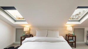 Ein Schlafzimmer mit Oberlicht, einem Bett, zwei Nachttischen mit Lampen und einem zusätzlichen Tisch.
