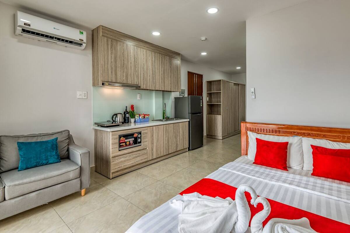 A hotel room with a bed, a sofa, a kitchenette, and a bathroom.
