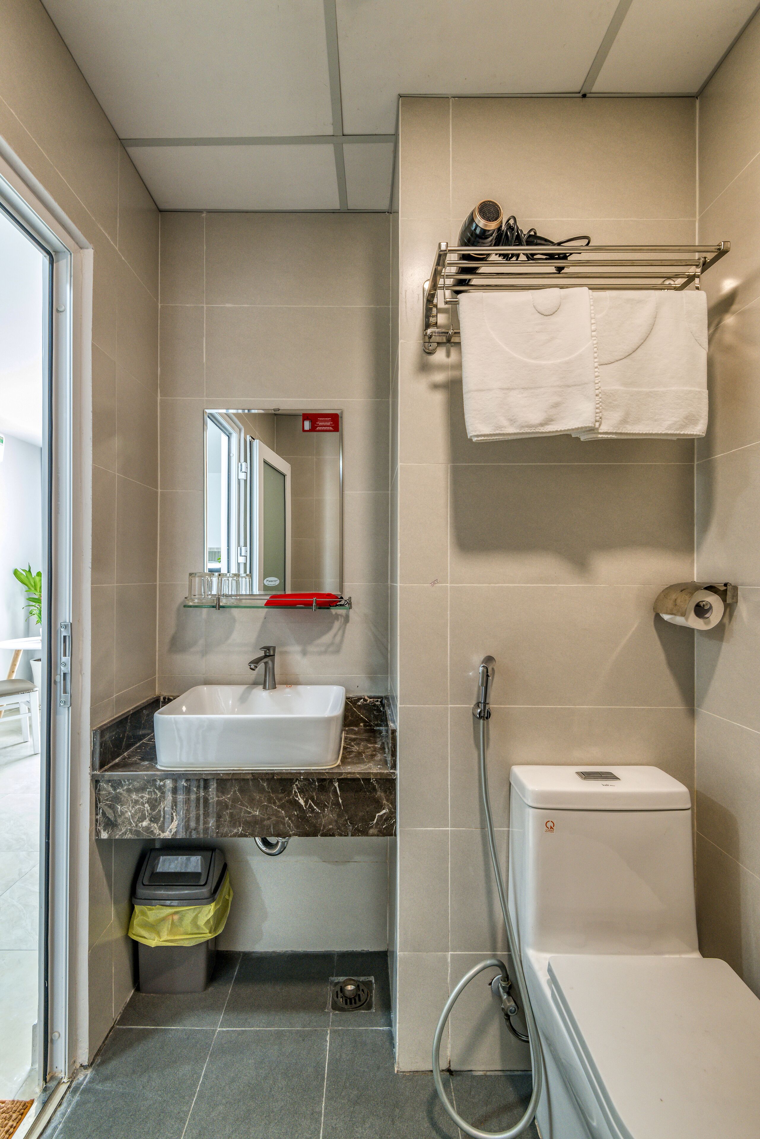 Une salle de bain équipée d’un lavabo, d’un miroir, d’un porte-serviettes, de toilettes et d’une poubelle.