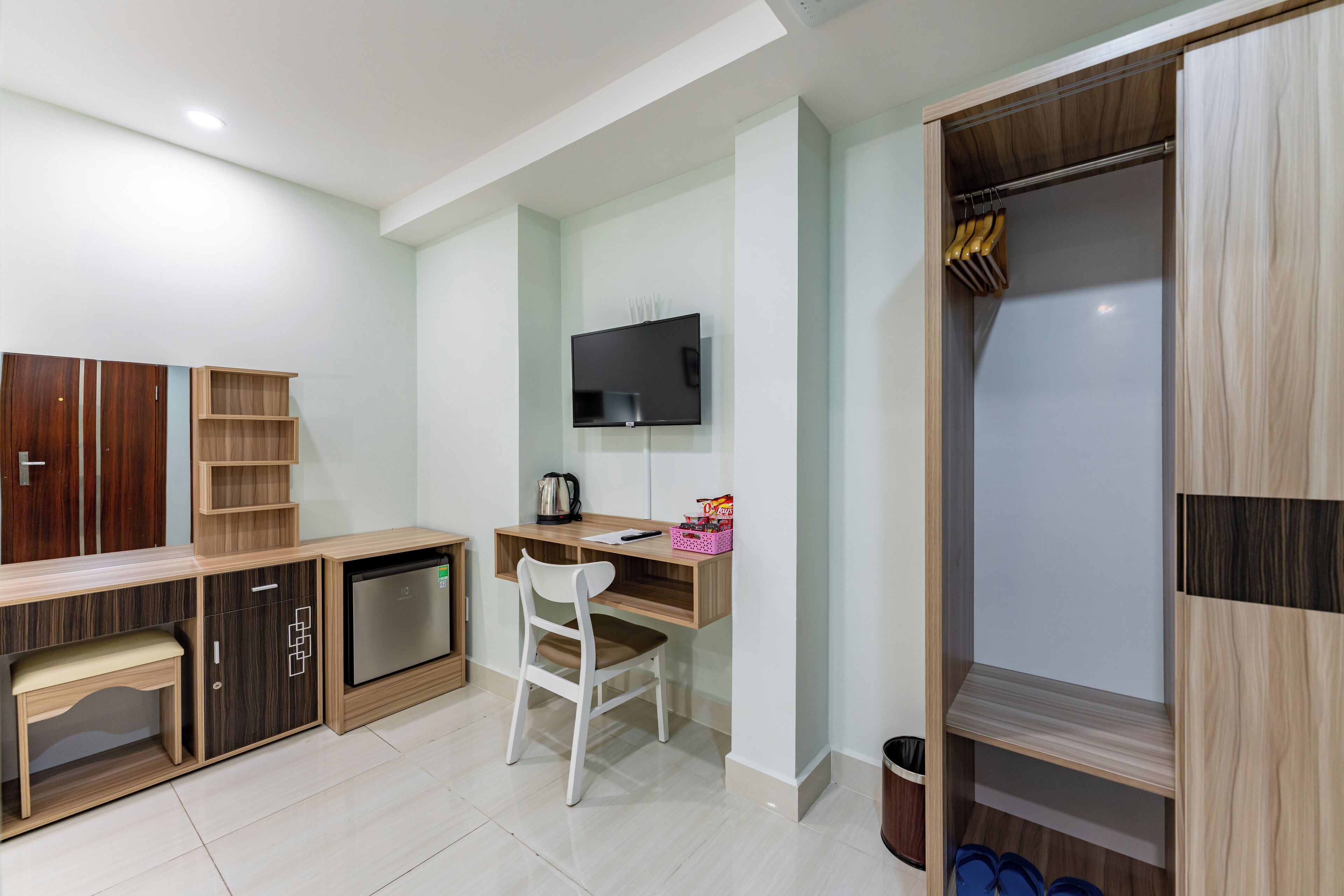 A modern room with a wooden desk, a television, a wardrobe, and a bench.
