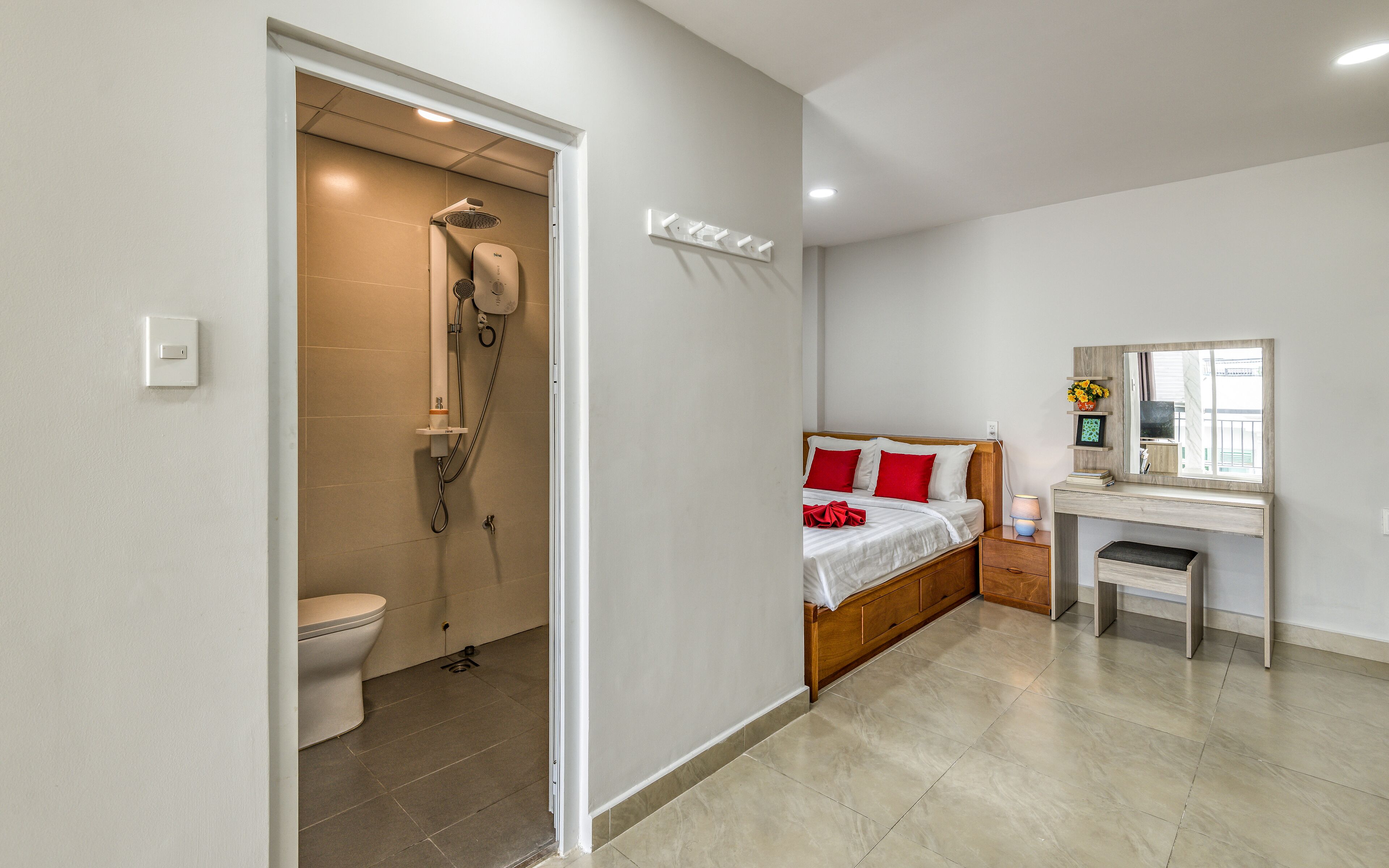 Habitación de hotel con ducha, inodoro, cama, mesita de noche y espejo.