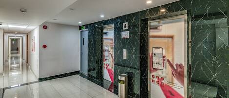 Eine Hotelhalle mit klarem, modernem Design, darunter ein Marmorboden, ein Empfangstresen und ein digitales Aufzugssignal.