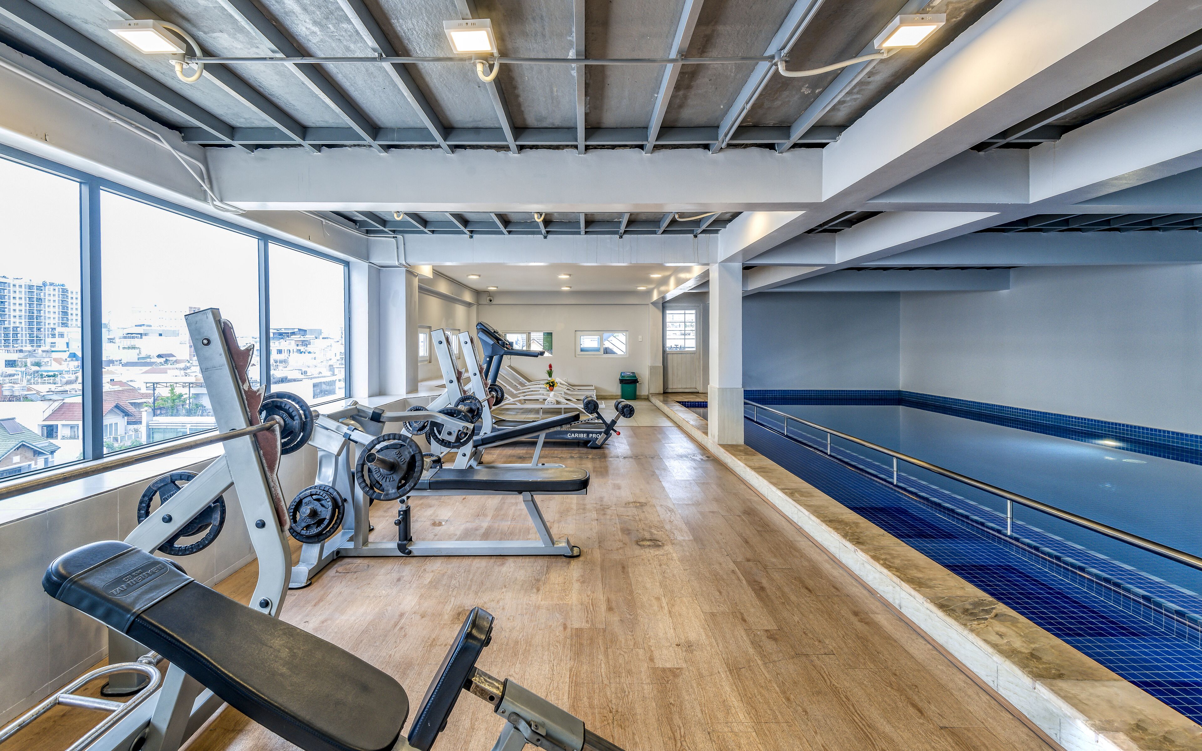 A gym with cardio machines, a pool, and large windows offering city views.