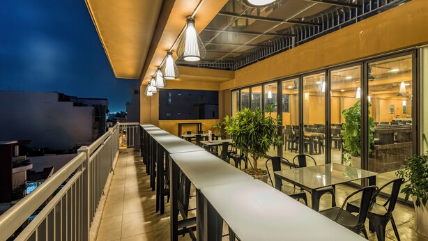 An outdoor dining area with tables and chairs, a railing, and potted plants.