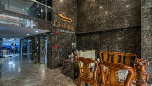 A hotel lobby with a marble reception desk, a wooden chair, and a sign reading "CHERRY Hotel & Apartment".