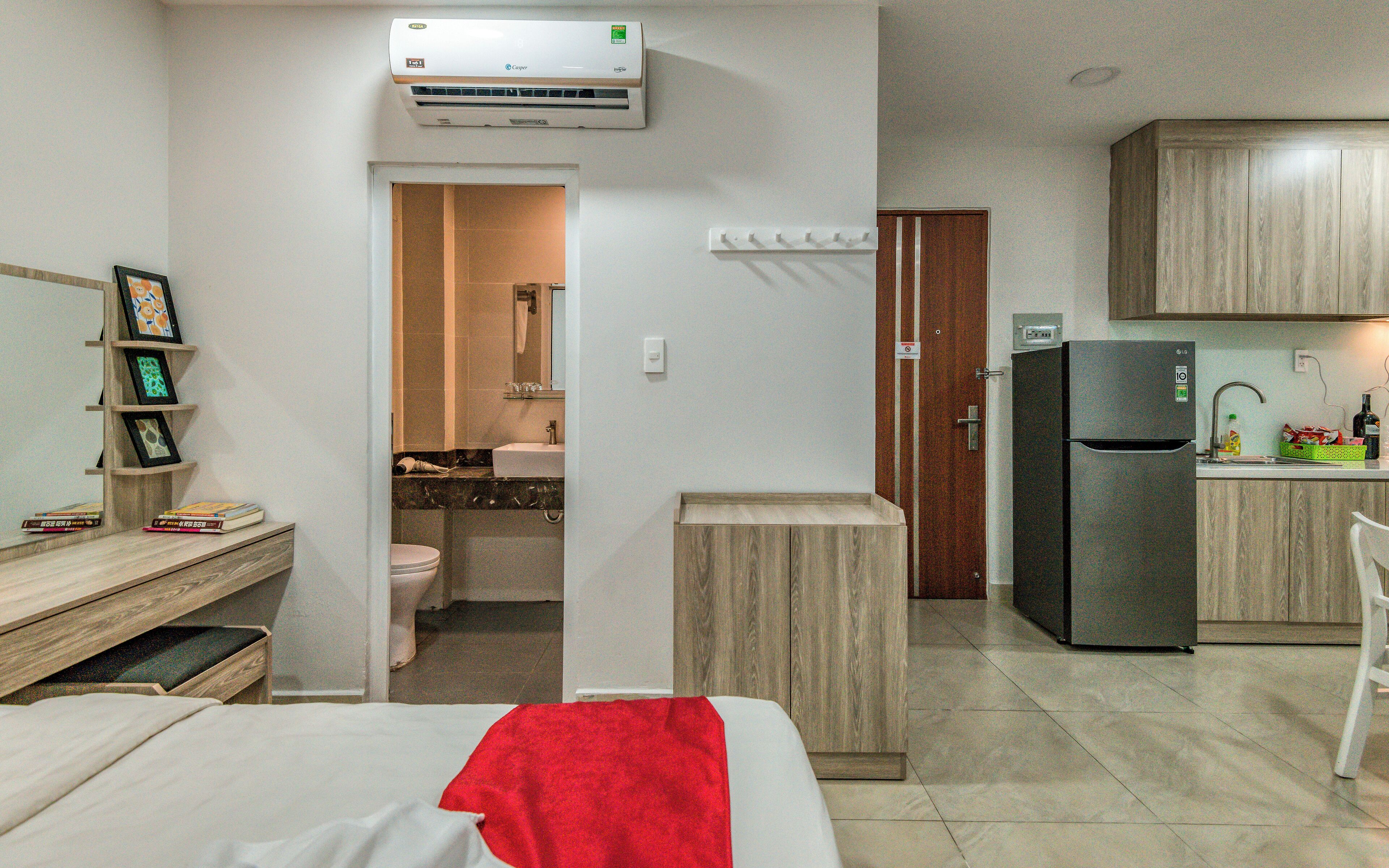 Camera d'albergo compatta con un letto, una scrivania, un angolo cottura e un bagno visibile tramite una porta aperta.