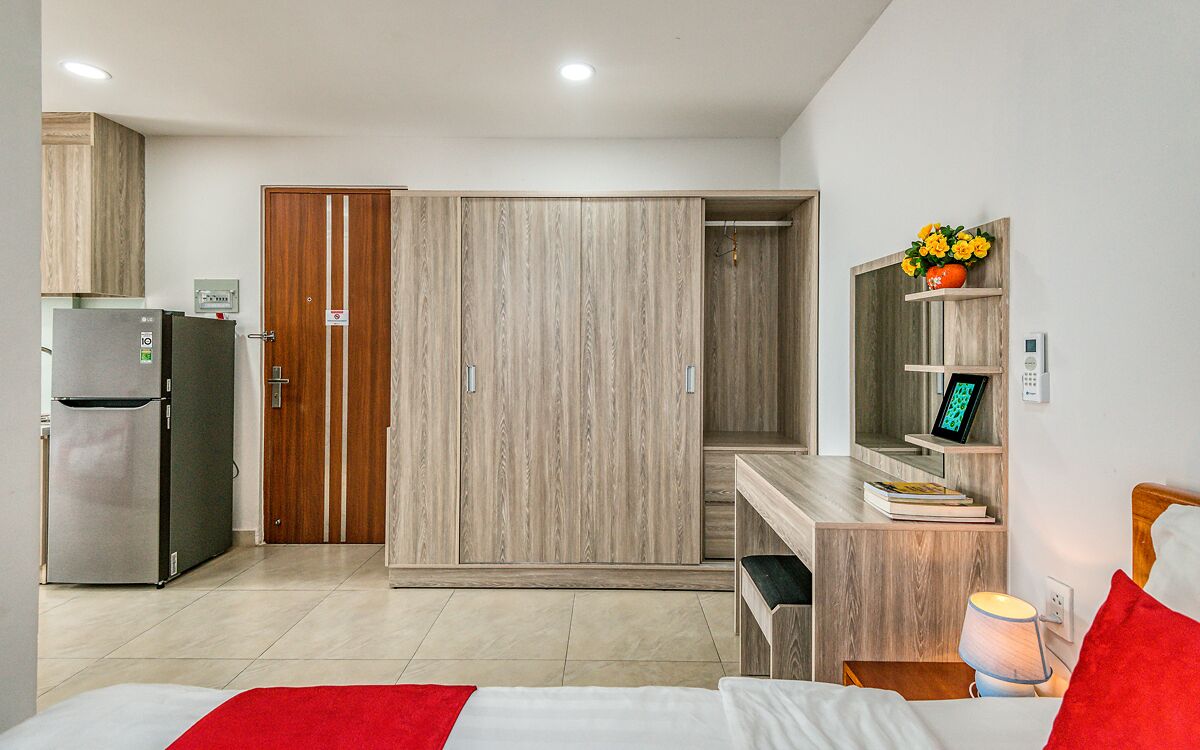 A hotel room with a bed, a desk, a wardrobe, a refrigerator, and a small kitchenette.
