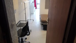 A hallway with a white wall, a wooden door, a black office chair, a white desk, and a white cabinet. - Les Effalées (THOLLON LES MEMISES)