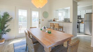 Un comedor amplio con una mesa de madera y sillas de mimbre, una lámpara colgante y vistas a la cocina y al balcón.
