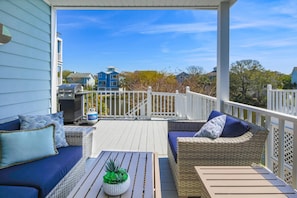 A covered outdoor deck with wicker furniture, a grill, and a view of neighboring houses.