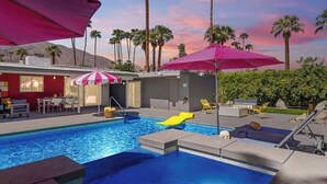 Uma piscina com escorregador, espreguiçadeiras e guarda-sóis.