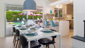 Uma cozinha moderna com uma ilha central, uma sala de jantar com mesa de vidro e vista para uma piscina.