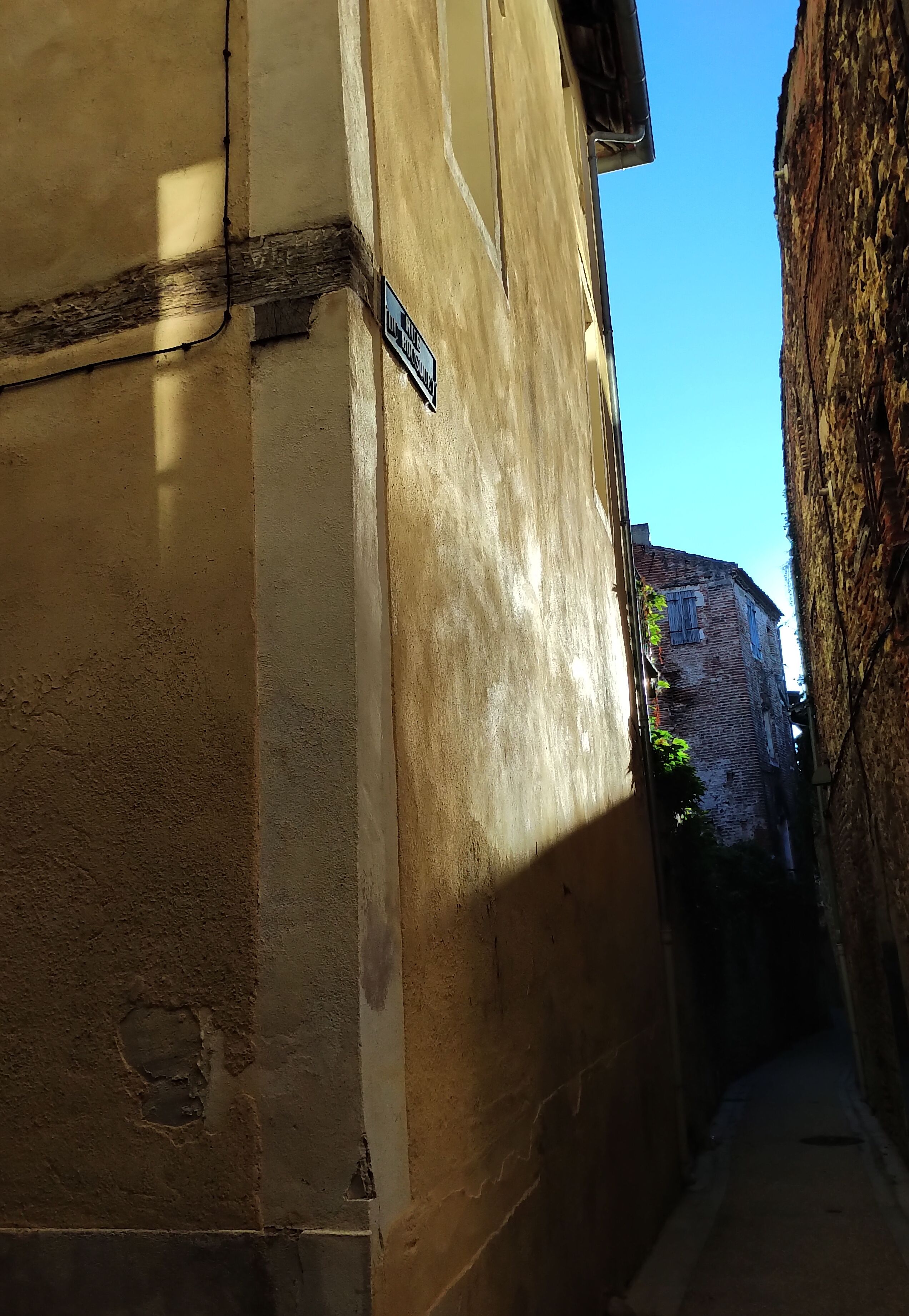 A narrow alleyway with a building on the left and a brick wall on the right.