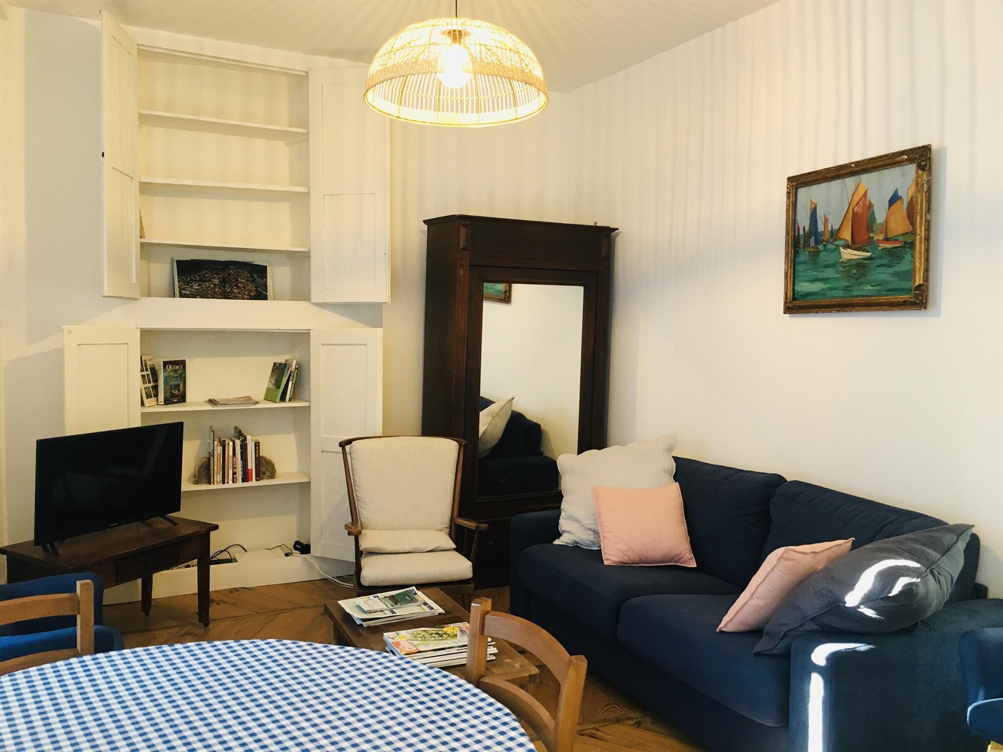 A living room with a blue sofa, a white armchair, a coffee table, a TV, and a bookshelf.