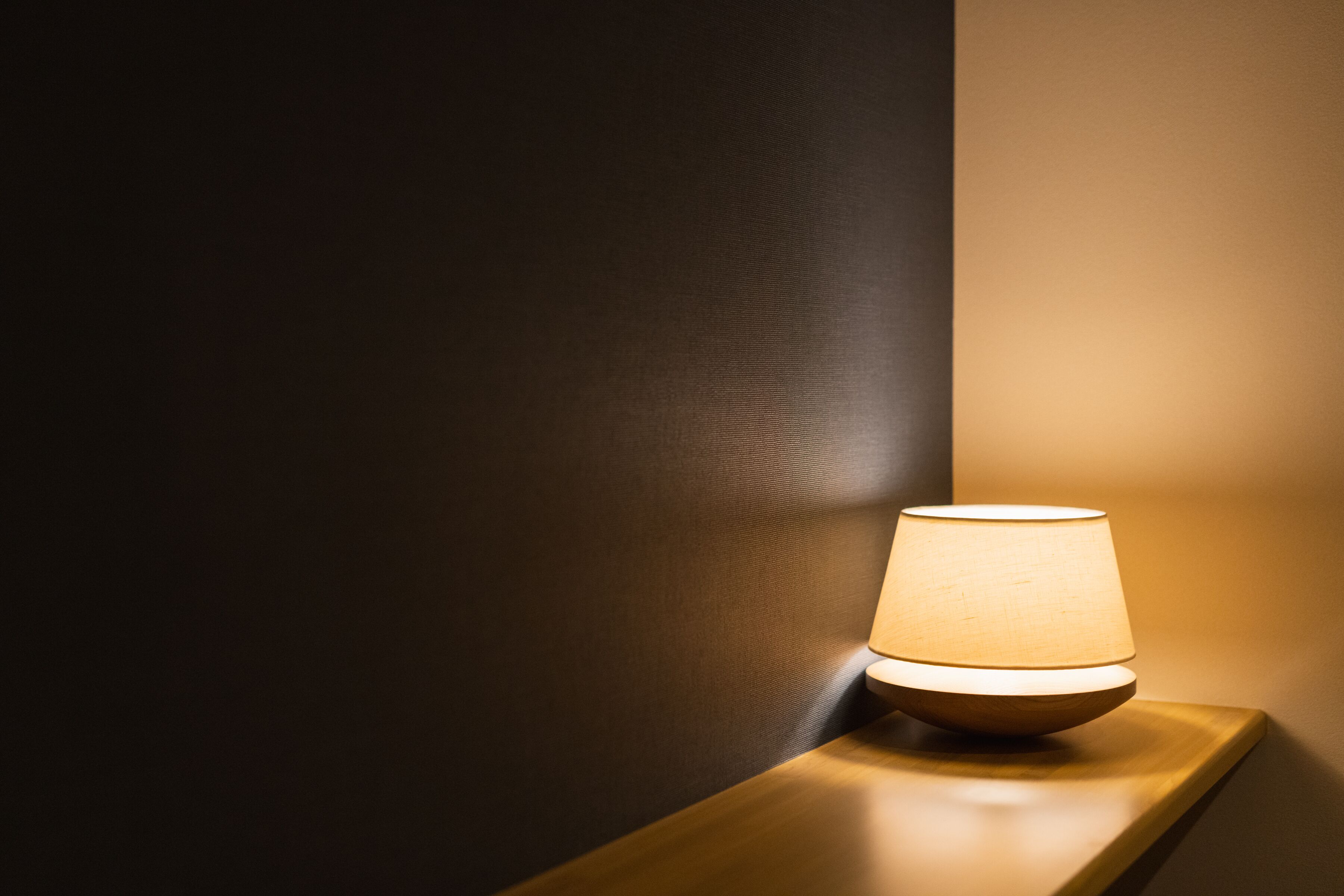 A table lamp on a wooden nightstand against a dark wall.