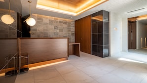 A modern reception area with a wooden reception desk, stone walls, and a tiled floor. - HOTEL All Stay Hakata Kuko Dori (Fukuoka)
