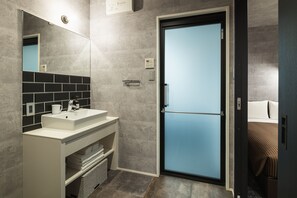 Un bagno moderno con un lavandino bianco, uno specchio e una porta in vetro satinato che dà accesso a una camera da letto.