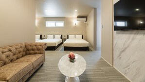 A hotel room with a sofa, two beds, a flat-screen TV, and a marble coffee table with flowers. - HOTEL All Stay Hakata Kuko Dori (Fukuoka)