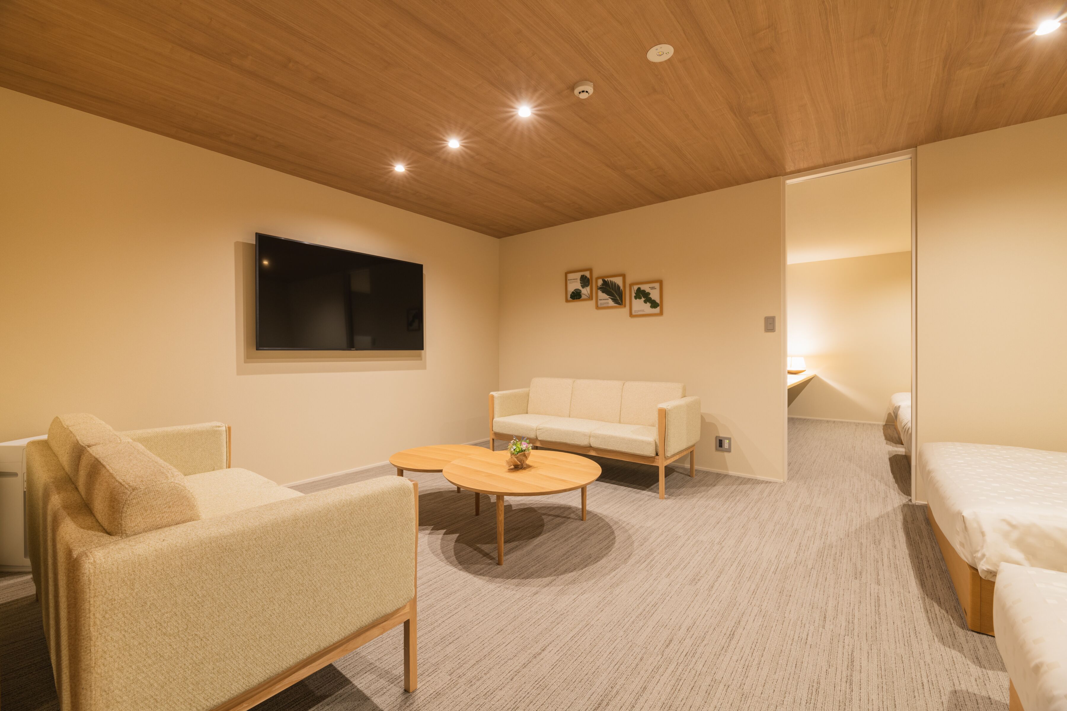 A modern hotel room with a wooden ceiling, a flat-screen TV, a sofa, a round coffee table, and a bed.