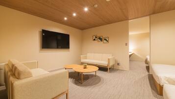 A modern hotel room with a wooden ceiling, a flat-screen TV, a sofa, a round coffee table, and a bed.