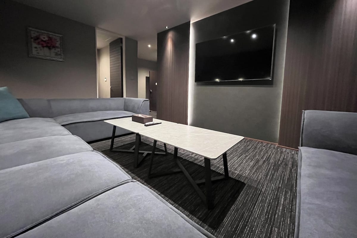 Un salon moderne avec un canapé d’angle gris, une petite table et un téléviseur à écran plat fixé au mur.