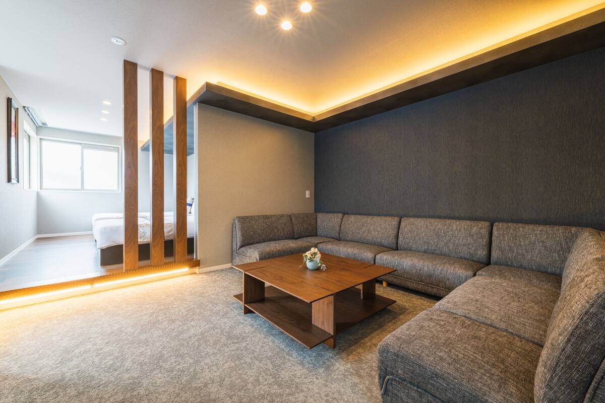 Un salon moderne avec un canapé d’angle, une table basse en bois et une grande fenêtre qui laisse entrer la lumière naturelle.