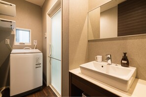 Een moderne badkamer met een wit wastafelmeubel, een spiegel en een inbouw raam boven de wastafel.