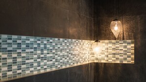 Une salle de bain moderne avec un mur recouvert de mosaïques et un luminaire suspendu.