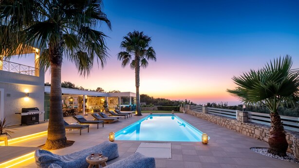 Zona de piscina con sillones de descanso, una piscina y vistas al atardecer.