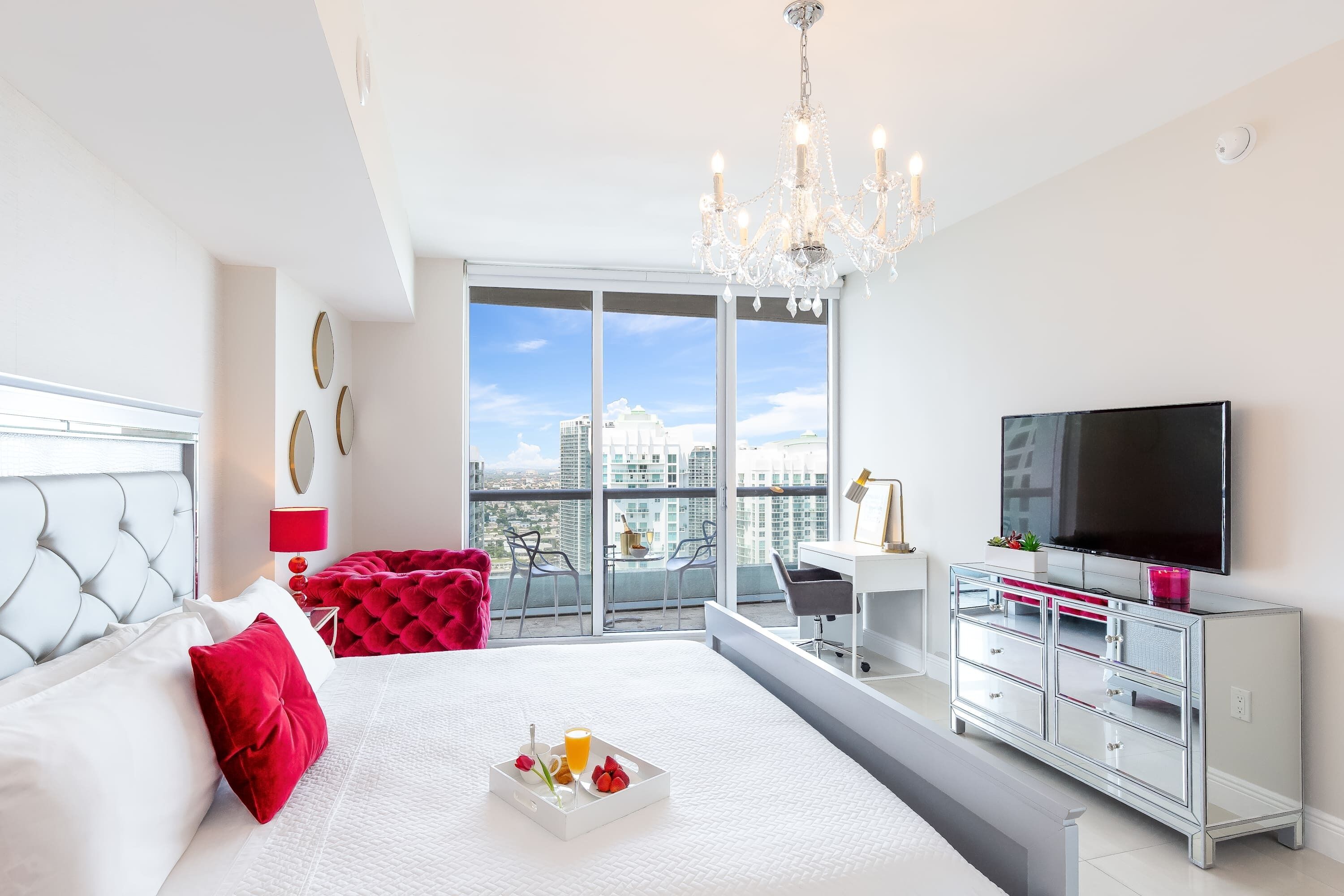 Ein modernes Hotelzimmer mit einem großen Bett, einem Fernseher, einem Balkon mit Stadtblick und einem Schreibtisch mit Stuhl.