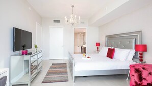 A modern bedroom with a large bed, a TV, a dresser, and a chandelier.
