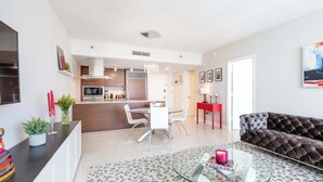 A modern living room with a glass coffee table, a sofa, and a dining area with a white table and chairs.