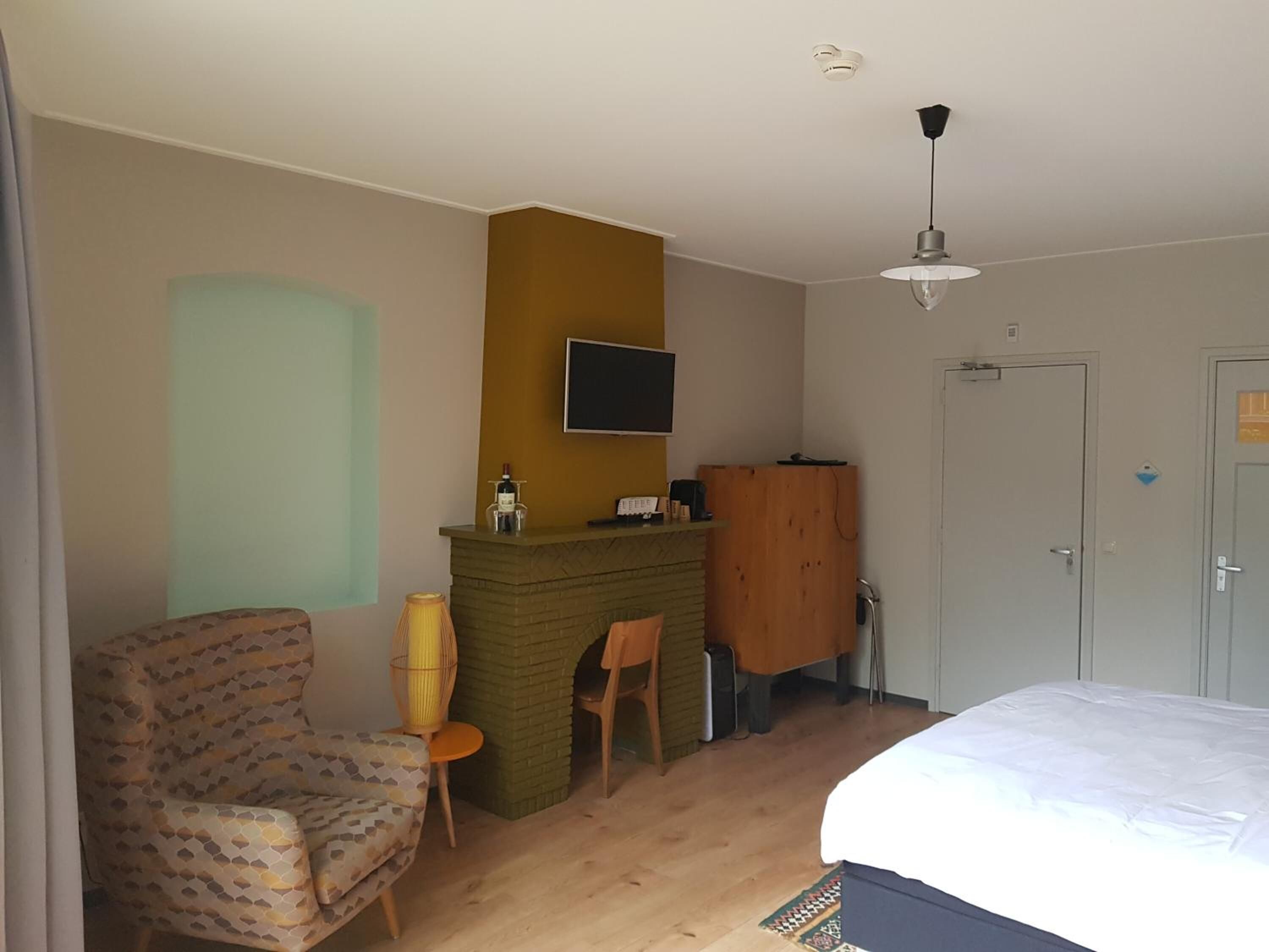 A hotel room with a bed, a chair, a small table, a fireplace, a TV, and a wardrobe.