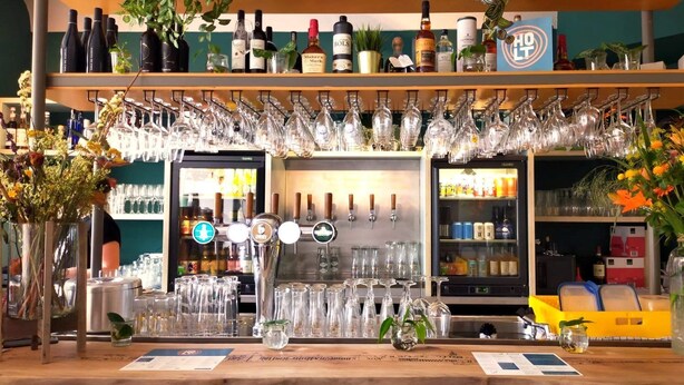 A bar area with multiple wine bottles, glasses, and a refrigerator stocked with beverages. - Holt Nijmegen (Nijmegen)