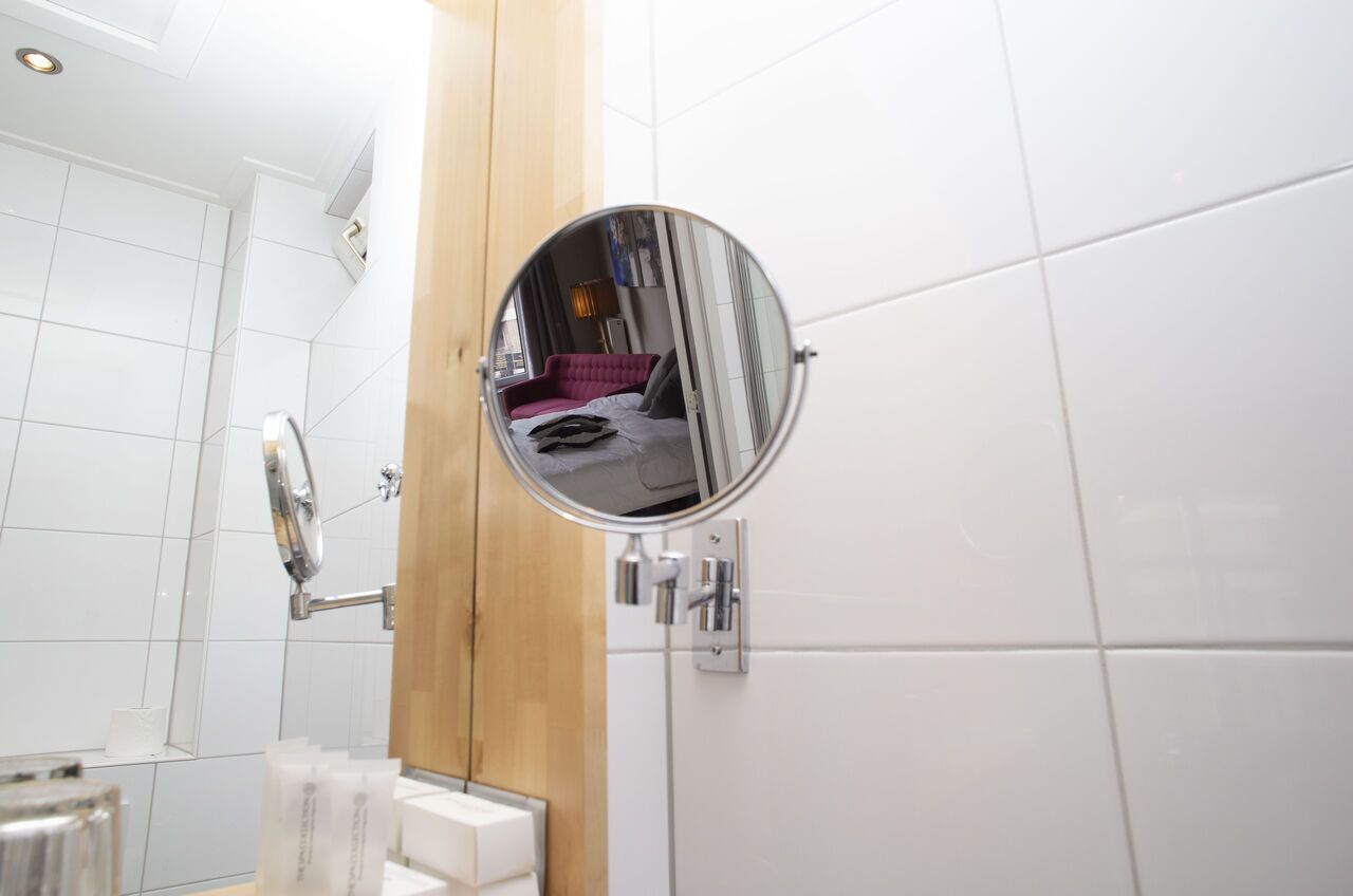 A bathroom with white tiles, a round mirror, and a wooden panel.