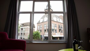 A room with a large window, a red chair, and a small table with a bottle and glass. - Holt Nijmegen (Nijmegen)