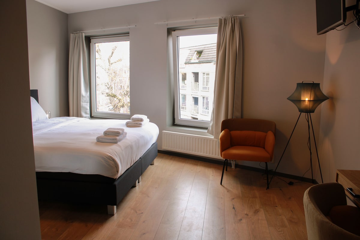 Un dormitorio con una cama, dos ventanas, una silla y una lámpara de pie.