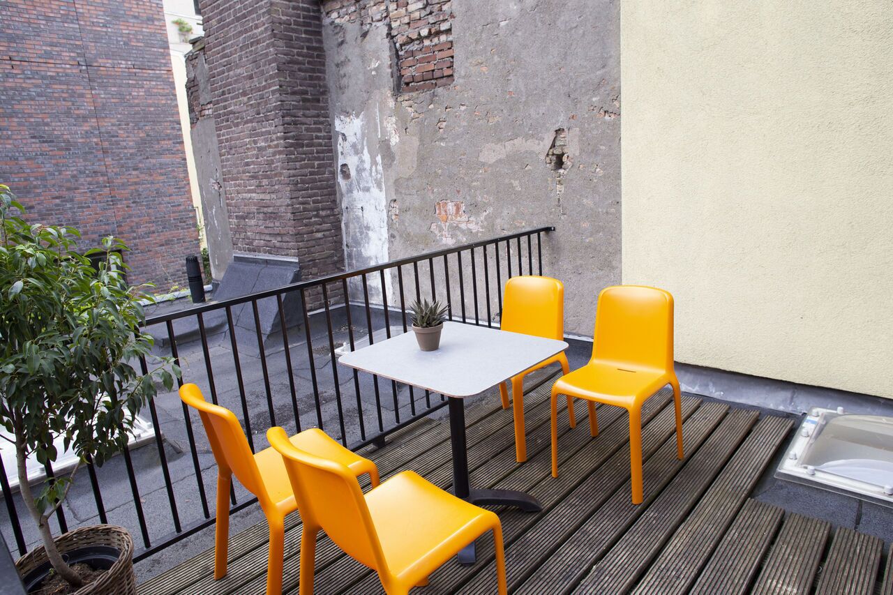 A small outdoor seating area with a table and four chairs, a potted plant, and a brick wall in the background.