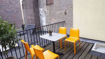 A small outdoor seating area with a table and four chairs, a potted plant, and a brick wall in the background.