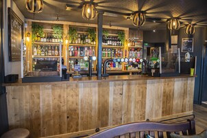 Una zona de bar con mostrador de madera, estantes con botellas de licores e iluminación colgante.