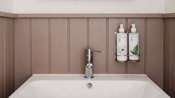 Un baño con un lavamanos blanco, un grifo cromado y dos botellas de champú en una estantería.