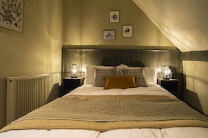 A bedroom with a large bed, two bedside tables with lamps, a radiator, and three framed pictures on the wall.