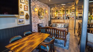 Um restaurante com parede de tijolos, móveis de madeira e um espaço de bar ao fundo.