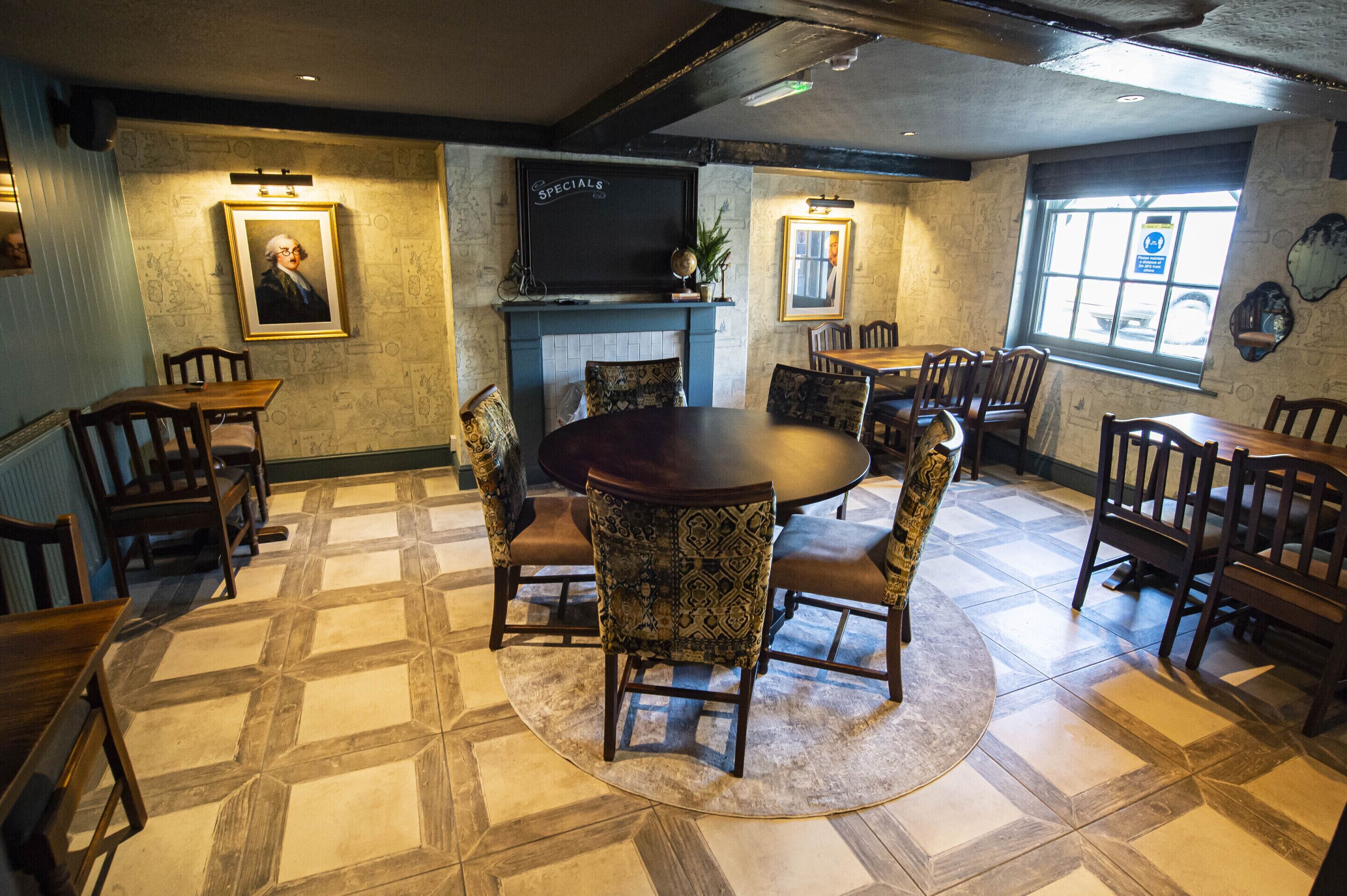 A dining area with a round table surrounded by chairs, a television mounted on the wall, and a patterned floor.
